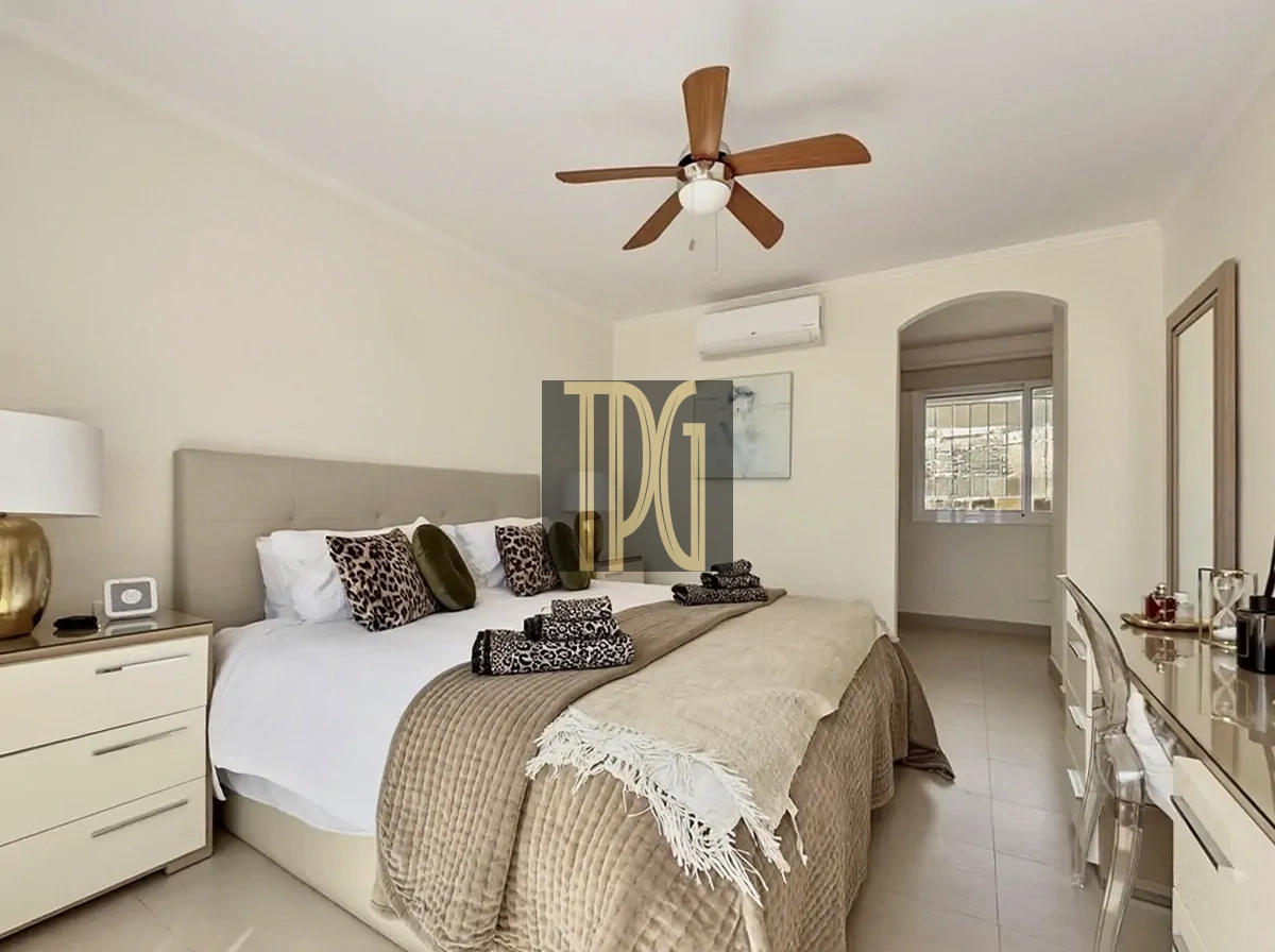 File 00011jpg Bright beige master bedroom with a king bed, leopard-print pillows, folded towels, and a ceiling fan above.
