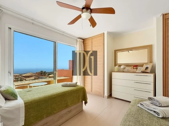 Twin-bed hotel room with olive-green bedspreads and a sea-view balcony through large glass doors