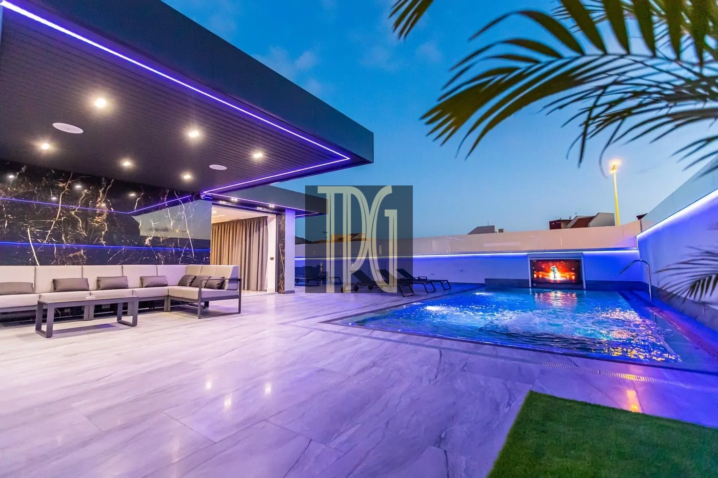 Luxurious rooftop terrace at dusk with purple LED lighting, beige sectional seating, and a rectangular pool with a wall-mounted screen.