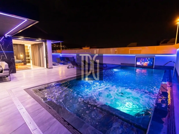 Rooftop pool at night with blue lighting, lounge chairs, and an open sliding-door living area visible to the left.