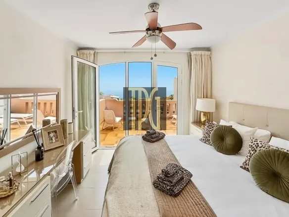 Bright hotel bedroom with a large bed, neutral bedding, and green round pillows, opening to a sunny balcony beyond.