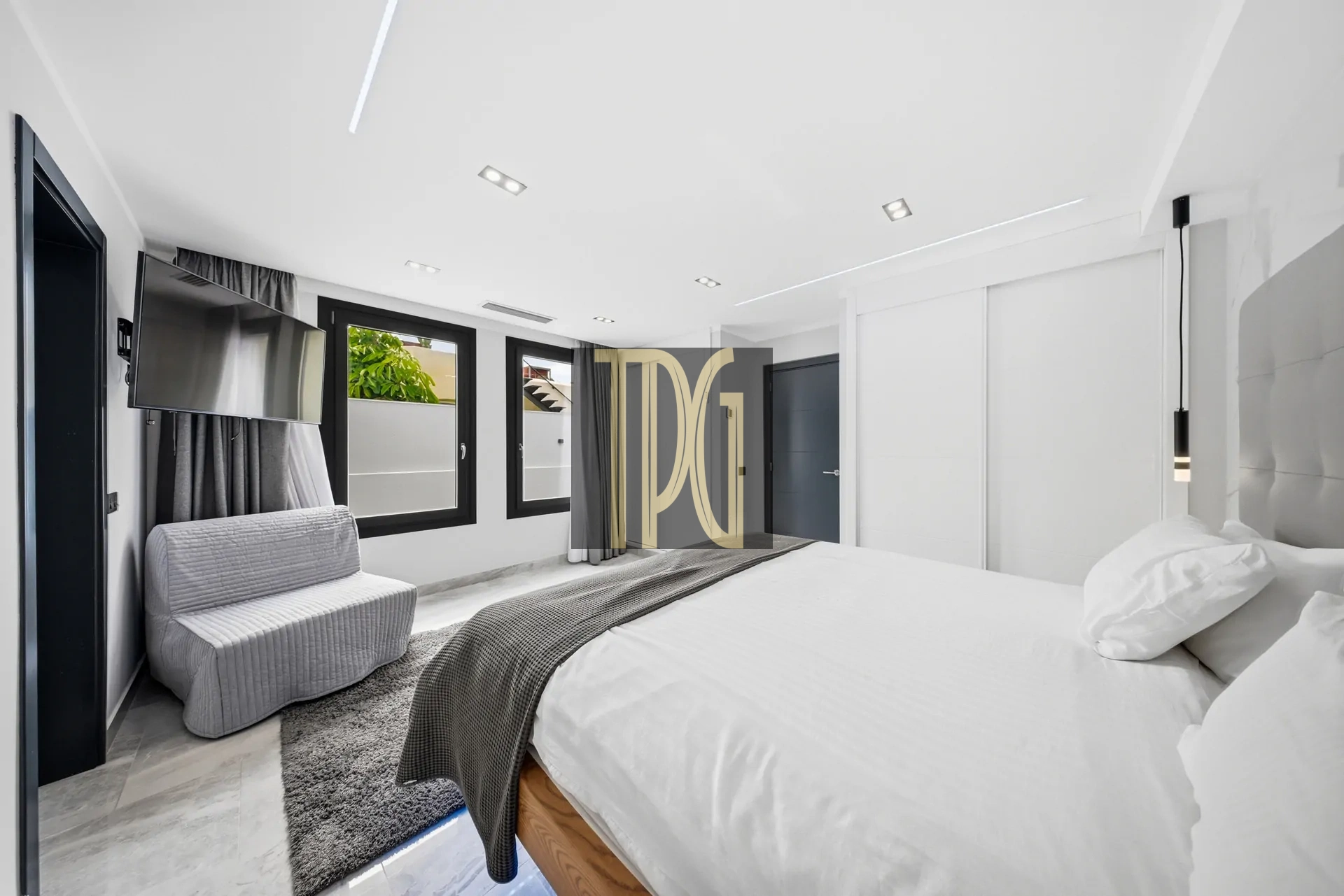 Modern white hotel bedroom with two beds, gray bedding, a wall-mounted TV, and large windows with black frames.",