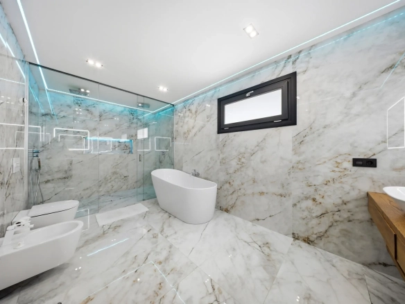 Luxurious marble bathroom with a glass-enclosed shower, freestanding oval tub, and a wooden vanity against marble walls.