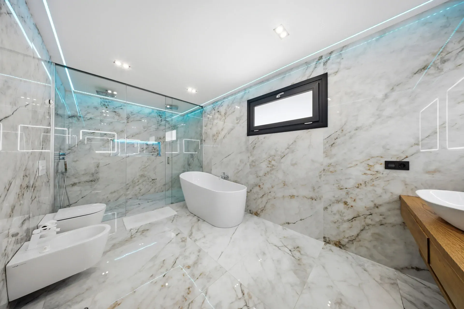 Luxurious marble bathroom with a glass-enclosed shower, freestanding oval tub, and a wooden vanity against marble walls.