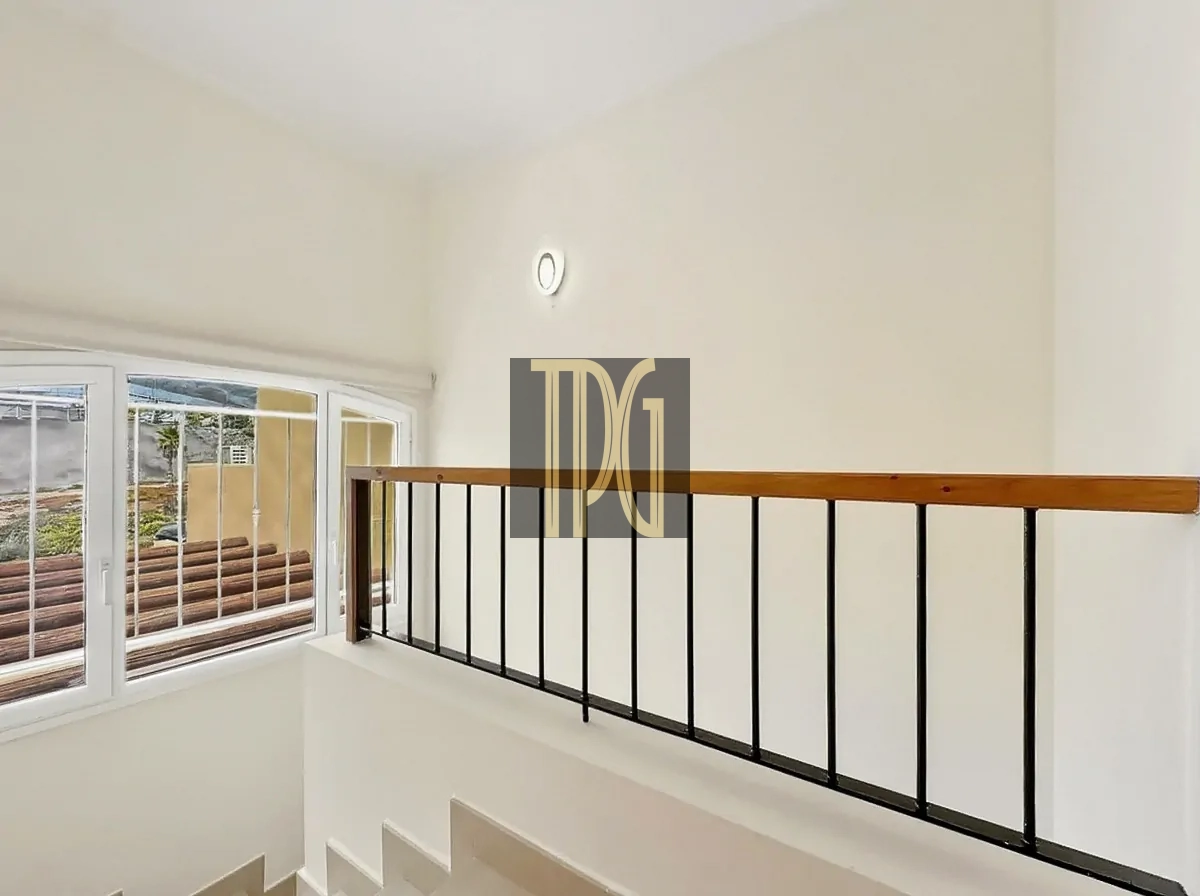 File 00019jpg Indoor stairwell with white walls, a wooden handrail, and black metal balusters, next to a large window with bars visible outside.