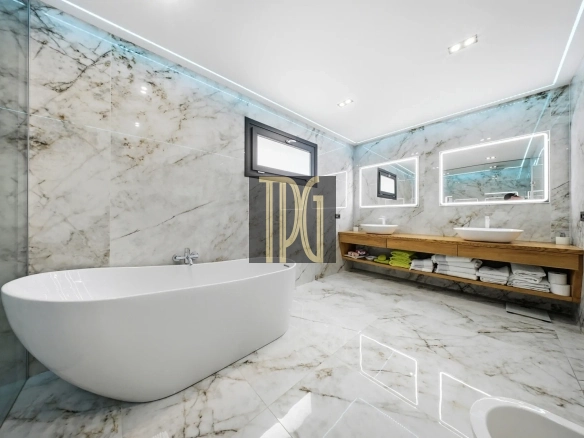 Luxurious marble bathroom with a freestanding white tub, glass shower, and double sinks on a wooden vanity.