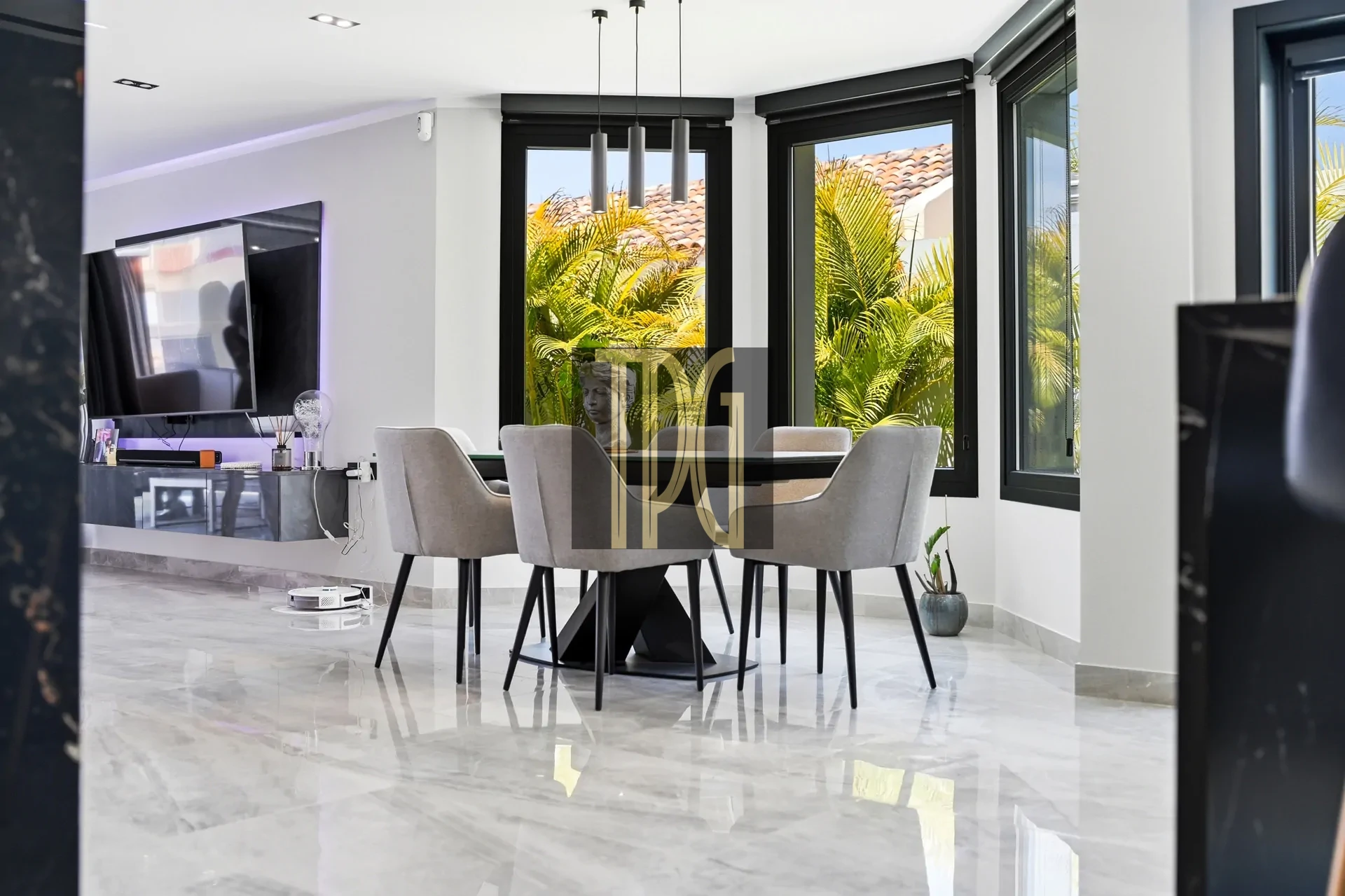 Contemporary dining room with a glass-top table, six gray chairs, and large windows with tropical plants outside.