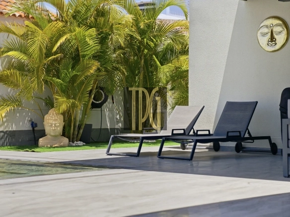 Poolside seating area with palm plants and a Buddha statue near the edge of a pool garden.