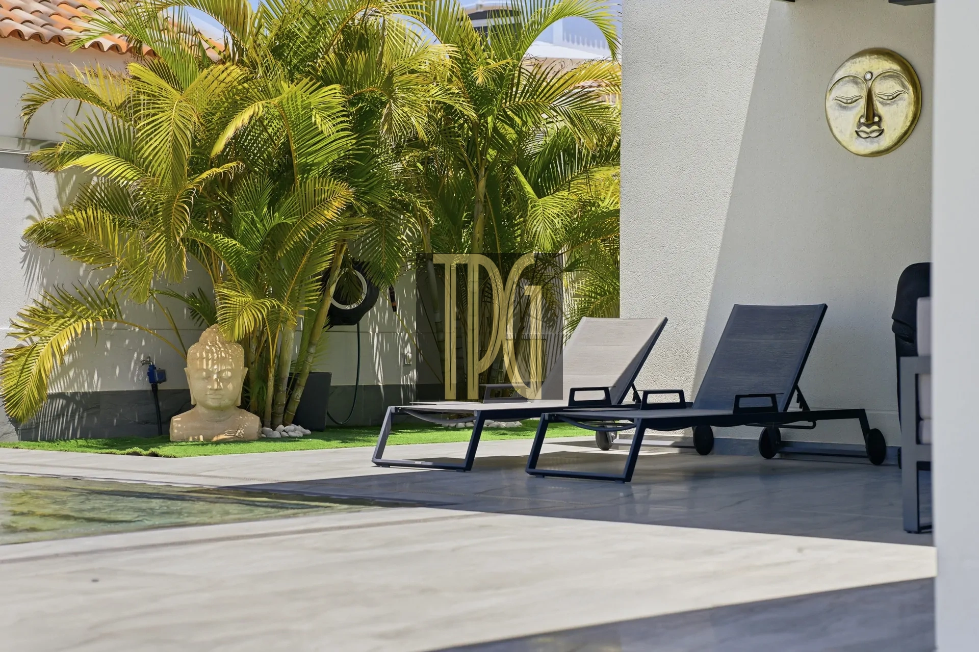 Poolside seating area with palm plants and a Buddha statue near the edge of a pool garden.