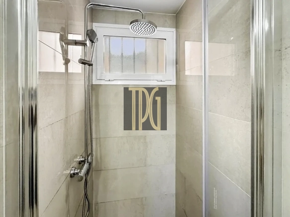 Modern glass-enclosed shower with a ceiling rainfall head, handheld wand, and tiled beige walls, plus a small window above.