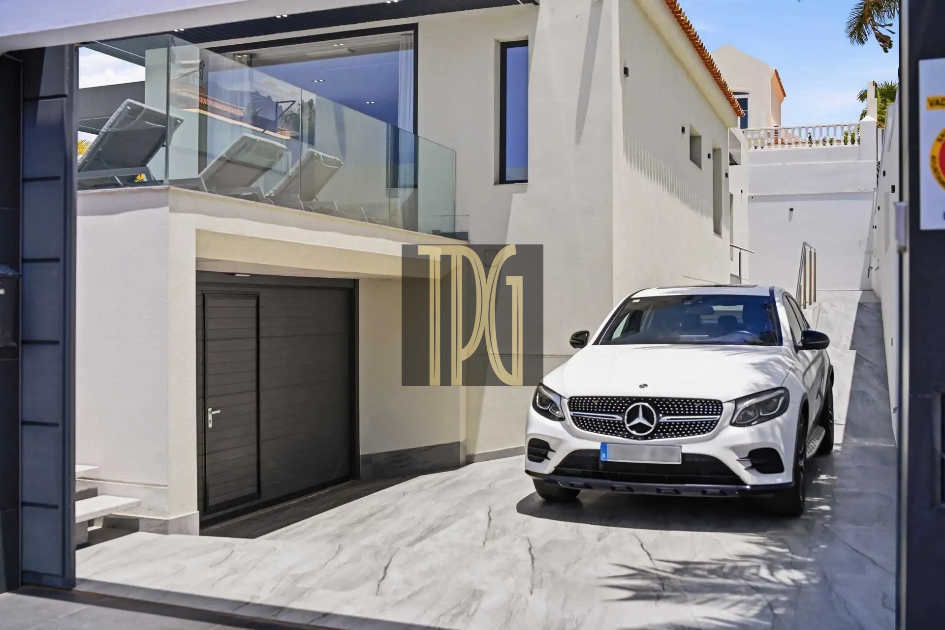White Mercedes SUV parked on a marble driveway in front of a modern white two-story house with a glass balcony.