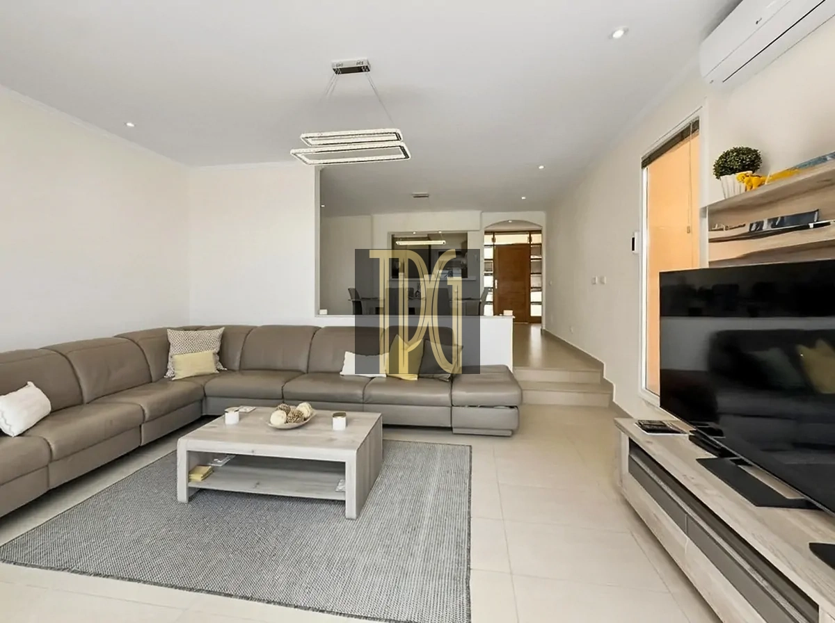 Modern living room with an L-shaped gray sectional sofa, light coffee table, rug, and a large flat-screen TV across from the seating area.] ,