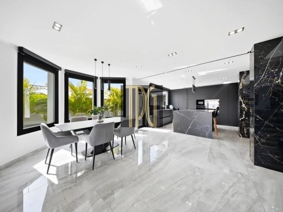Open-plan kitchen and dining area with marble floors, grey cabinetry, and large windows overlooking greenery outside.