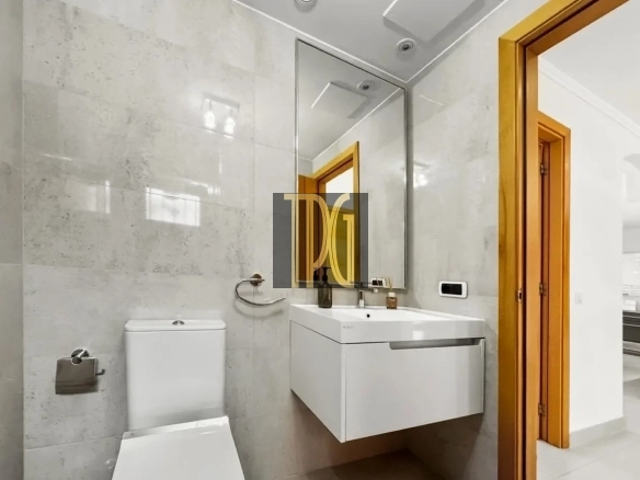 Modern bathroom with white vanity sink, large mirror, wall-mounted cabinet, and toilet next to a towel ring and toilet paper holder.