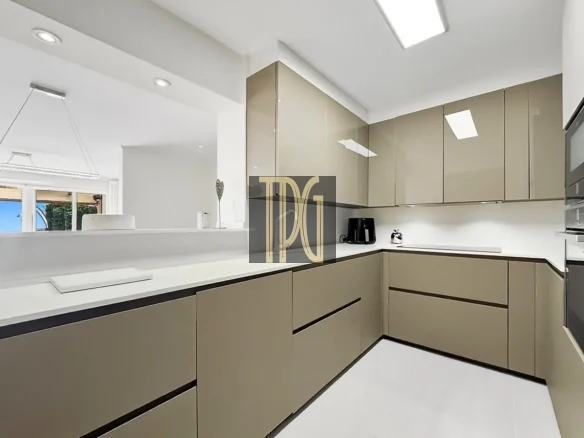 Modern beige L-shaped kitchen with white countertops and built-in cabinets, clean lines, and bright overhead lighting