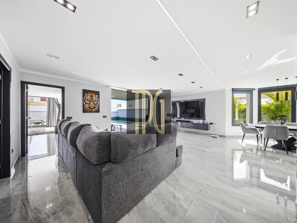 Open-plan living room with a grey sectional sofa, wall-mounted TV, and marble floors.