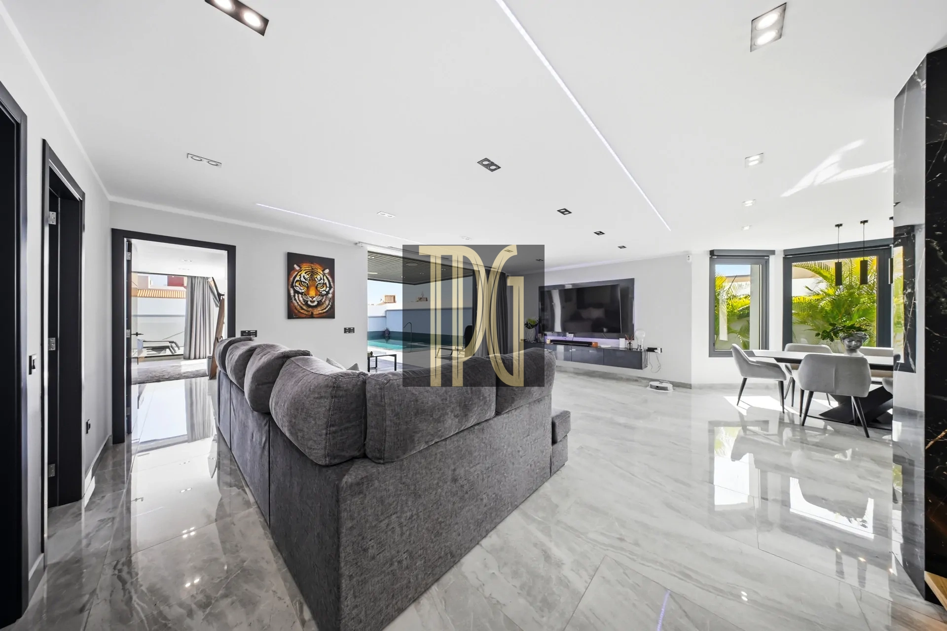 Open-plan living room with a grey sectional sofa, wall-mounted TV, and marble floors.