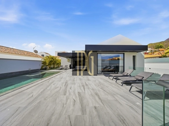 Modern villa backyard with a rectangular pool, lounge chairs, glass railing, and a blue sky above.