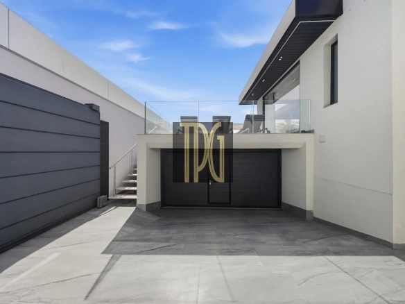 Modern white house with a dark garage door, glass balcony, and blue sky above.