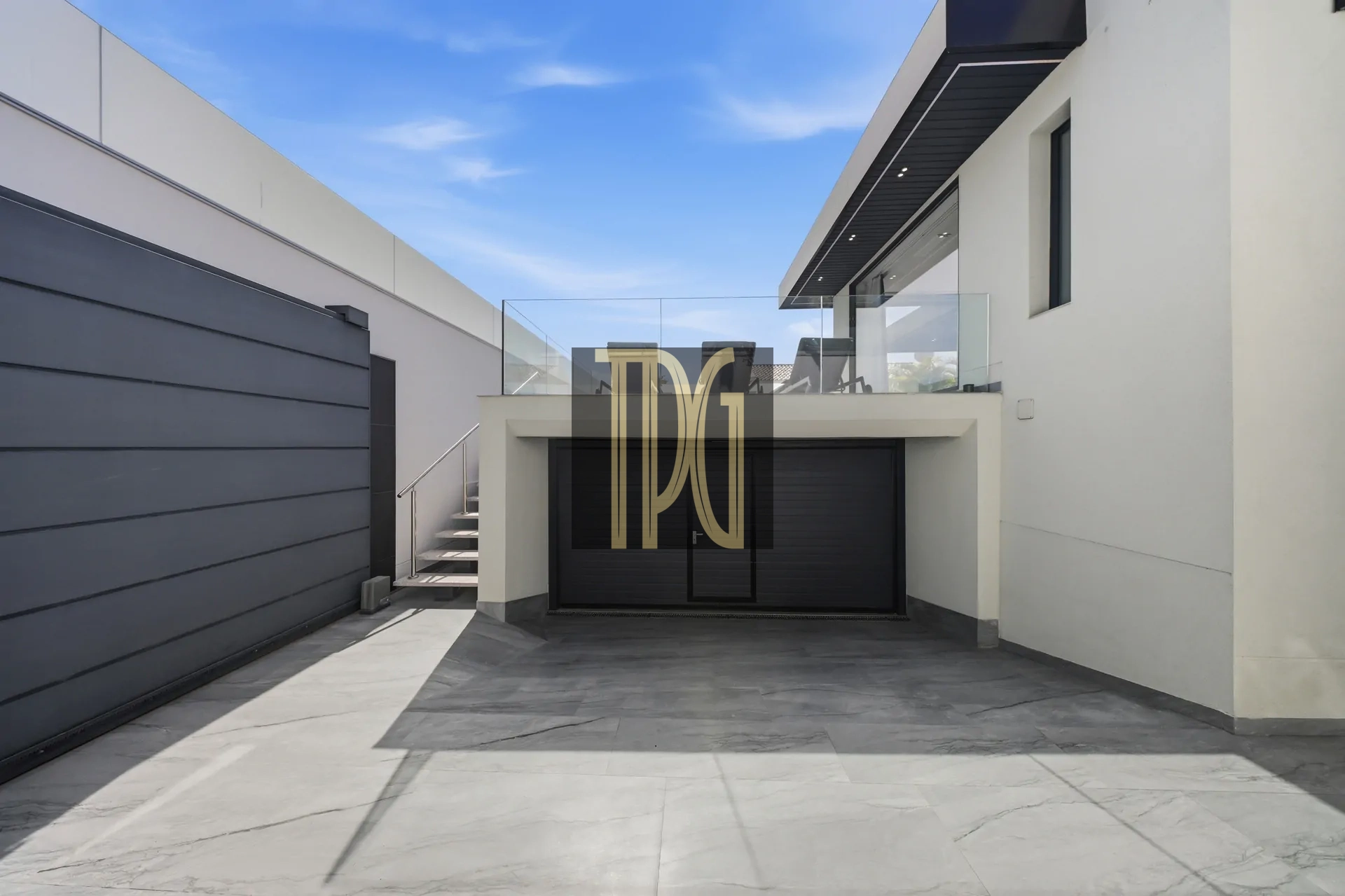Modern white house with a dark garage door, glass balcony, and blue sky above.