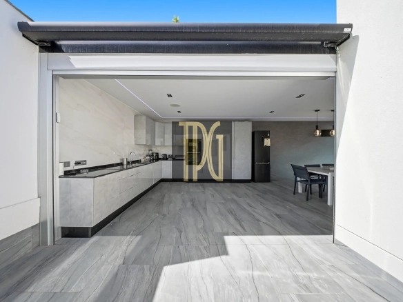Open garage door reveals a modern, open-concept kitchen with white cabinets, gray marble floors, and a dining area in the back.