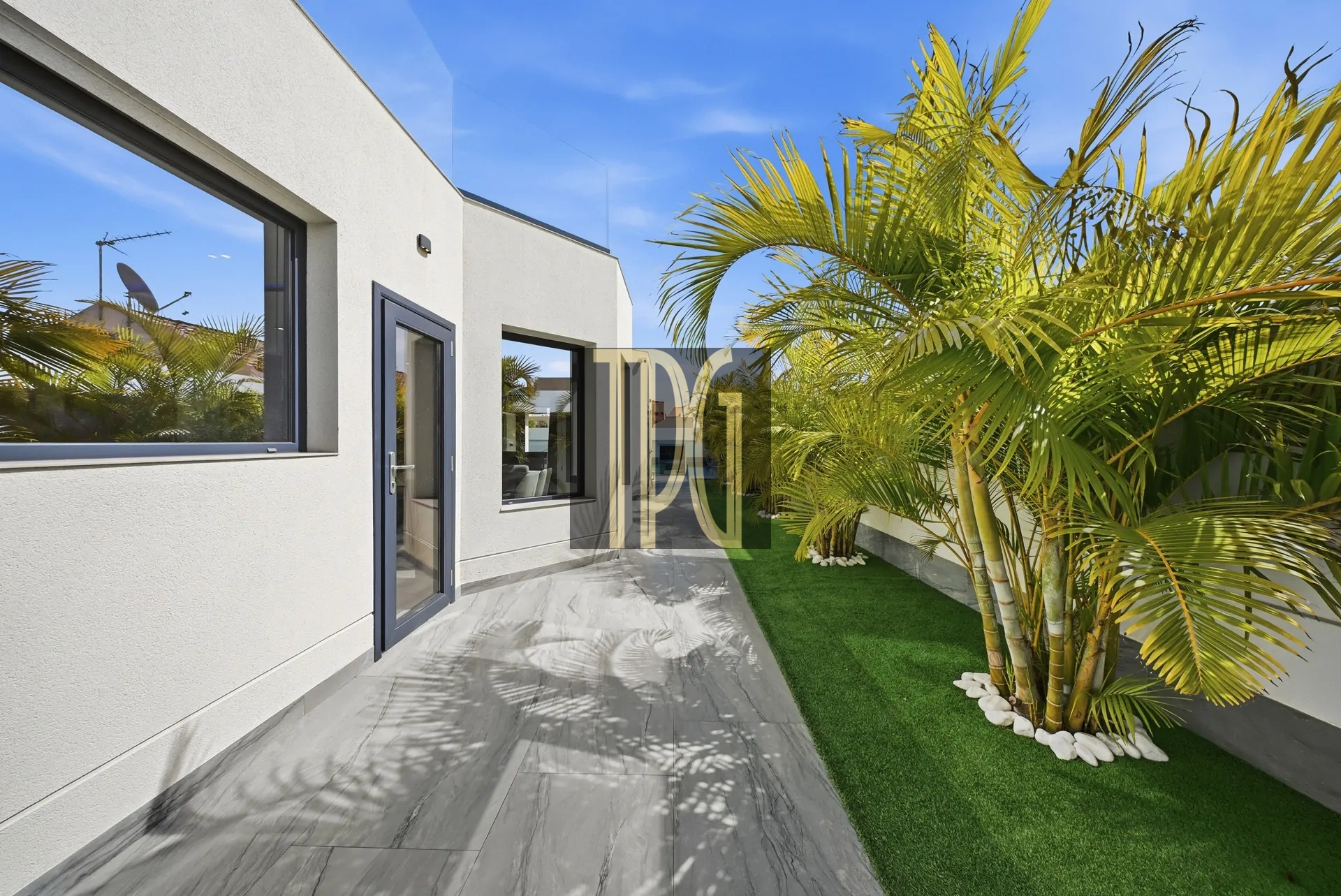 Modern white house exterior with gray-framed doors and windows, a tiled walkway, and tall palm trees along a manicured lawn, under a blue sky.