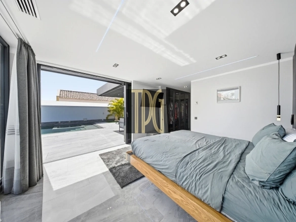 Bright modern bedroom with sliding glass doors opening to a pool deck and outdoor seating area outside the room.