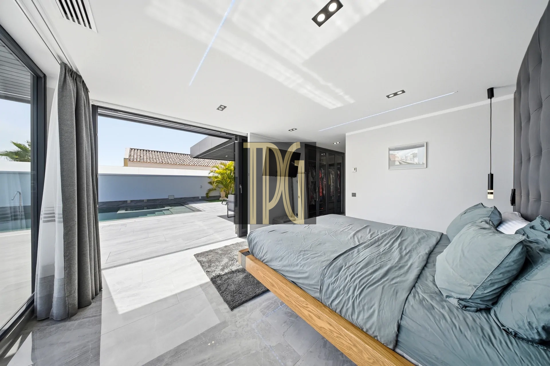 Bright modern bedroom with sliding glass doors opening to a pool deck and outdoor seating area outside the room.