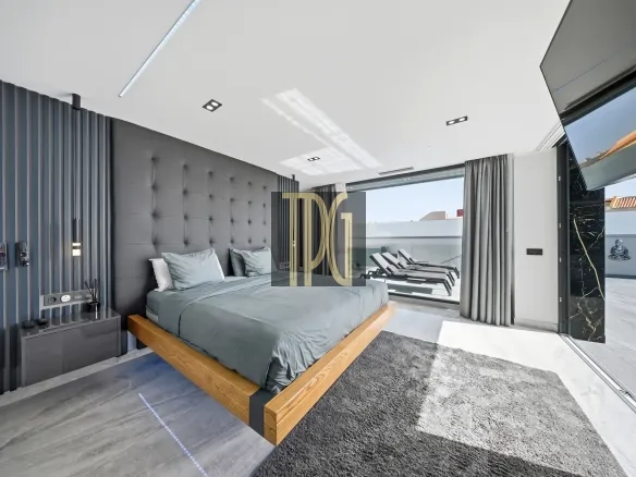 Modern bedroom with a low wooden platform bed, gray tufted headboard, and dark accent wall; large windows open to an outdoor lounge area