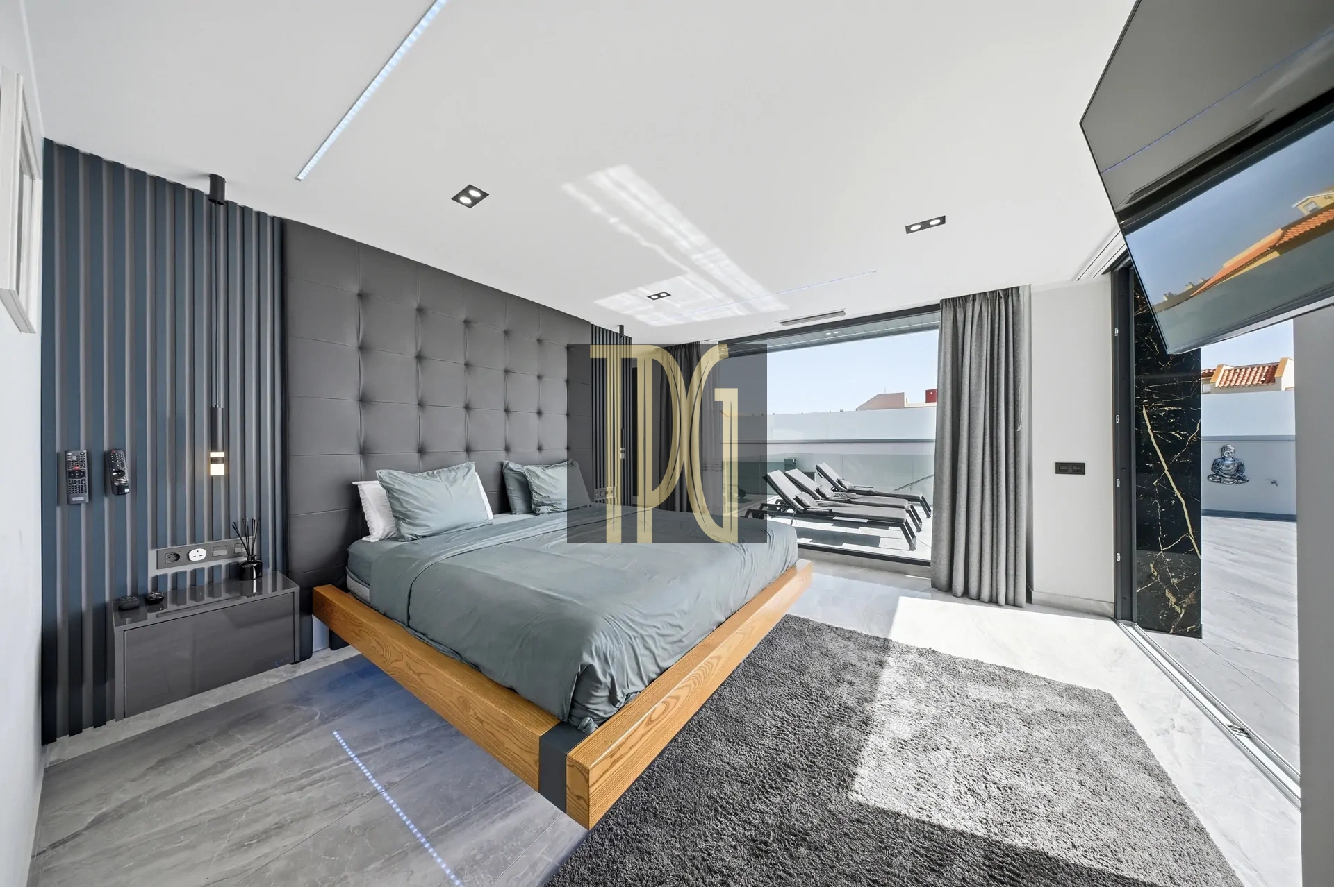 Modern bedroom with a low wooden platform bed, gray tufted headboard, and dark accent wall; large windows open to an outdoor lounge area
