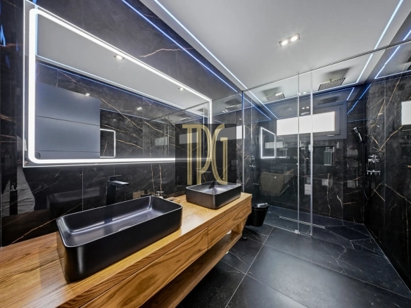 Luxurious black marble bathroom with a wood vanity and two black vessel sinks under a framed LED mirror.