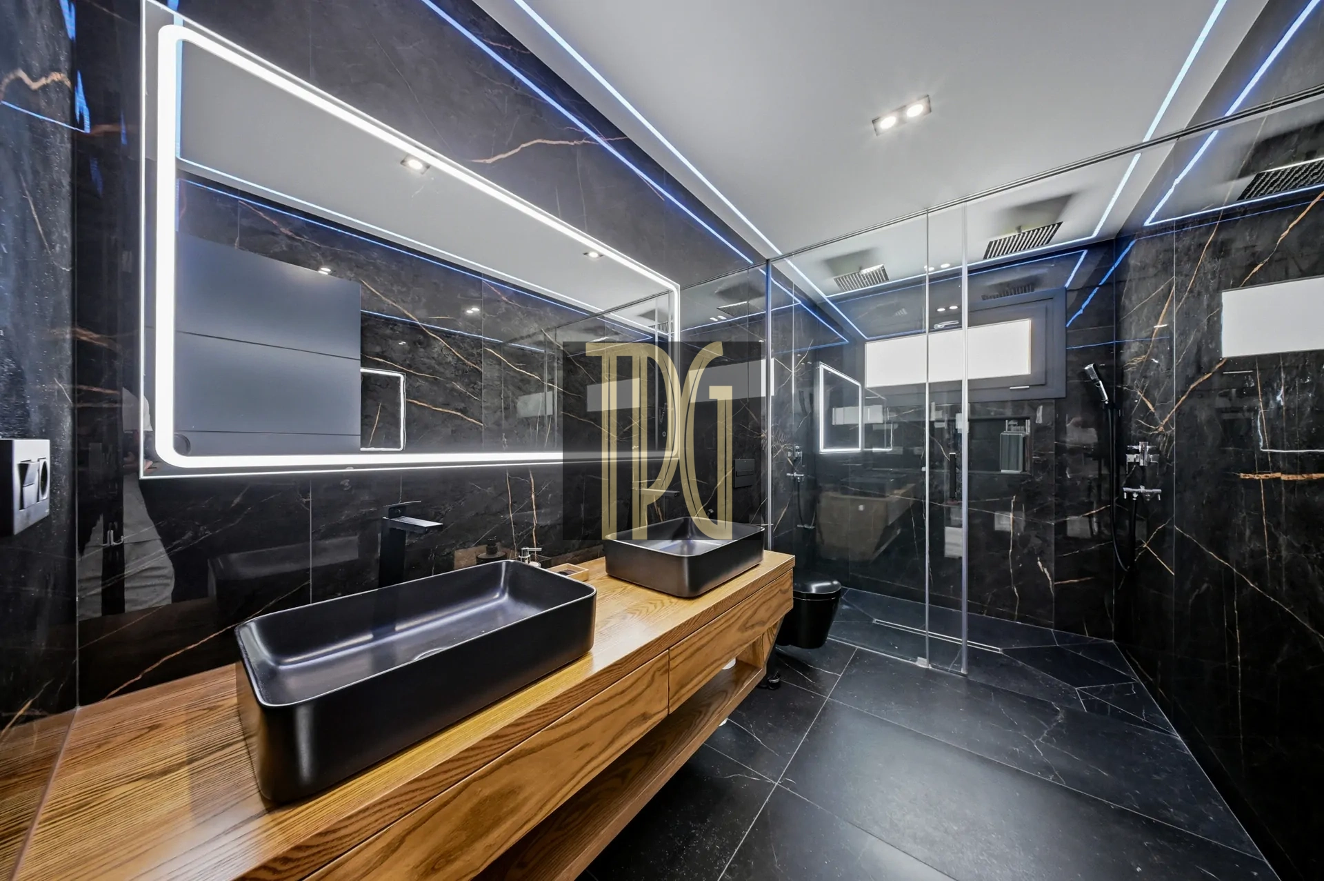 Luxurious black marble bathroom with a wood vanity and two black vessel sinks under a framed LED mirror.