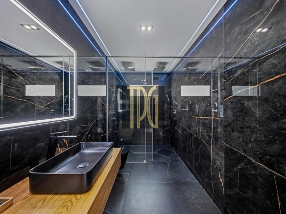 Modern bathroom with black marble walls, glass shower, and a wooden vanity with a black rectangular sink.