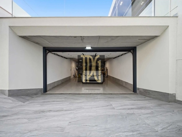 Open garage with a white car parked inside, viewed from the outside showroom-like entrance, marble driveway in foreground