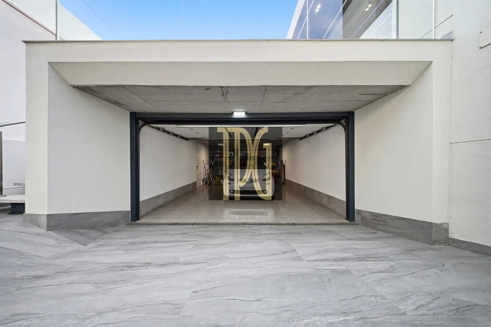 Open garage with a white car parked inside, viewed from the outside showroom-like entrance, marble driveway in foreground