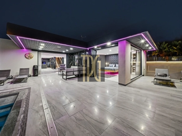 Night view of a modern backyard with a glass-walled living area, purple LED accents along the roof, and lounge chairs on a tiled patio.