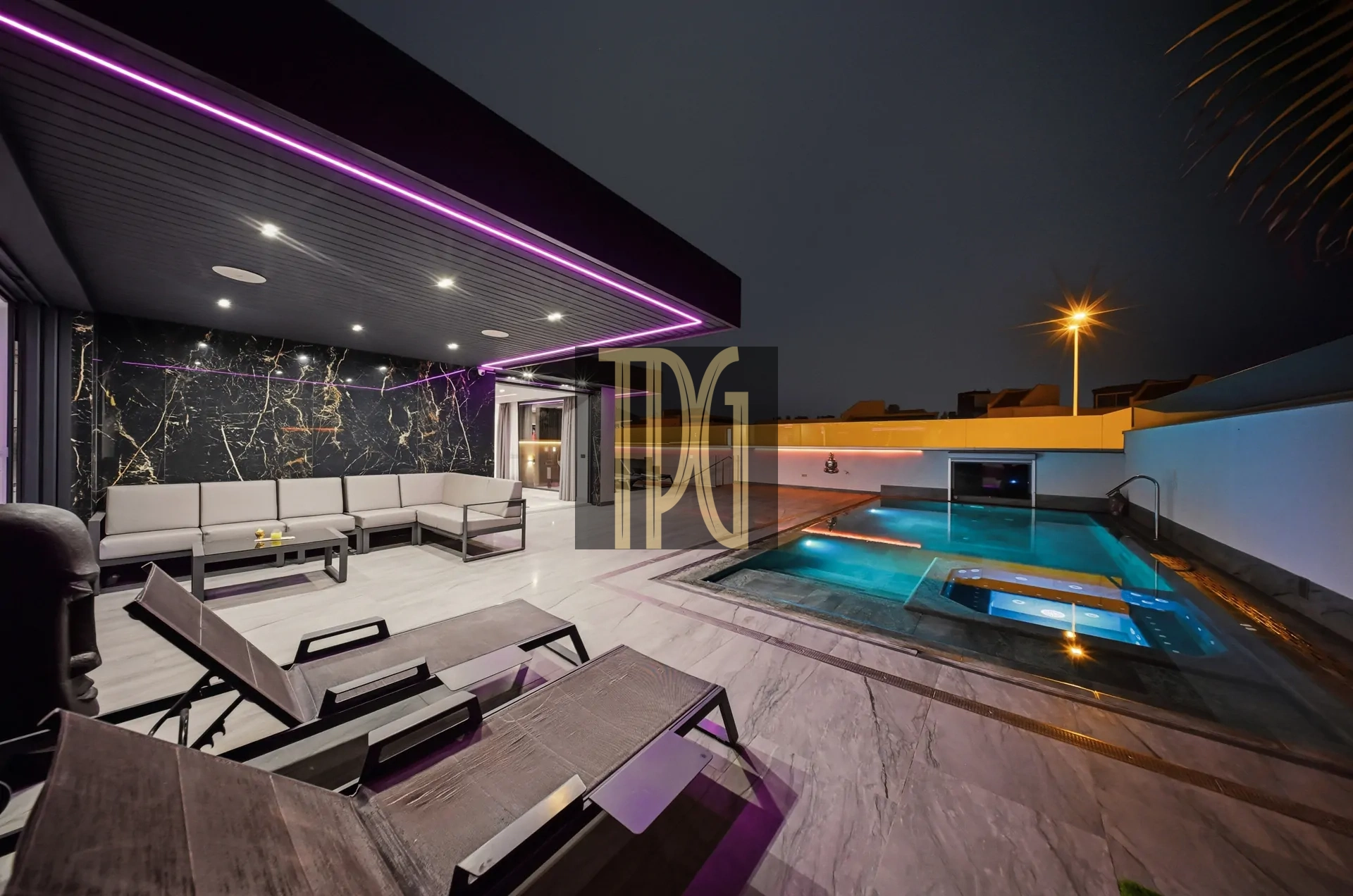Modern outdoor lounge at night with white sectional seating, marble wall, and purple LED lighting by a illuminated pool.