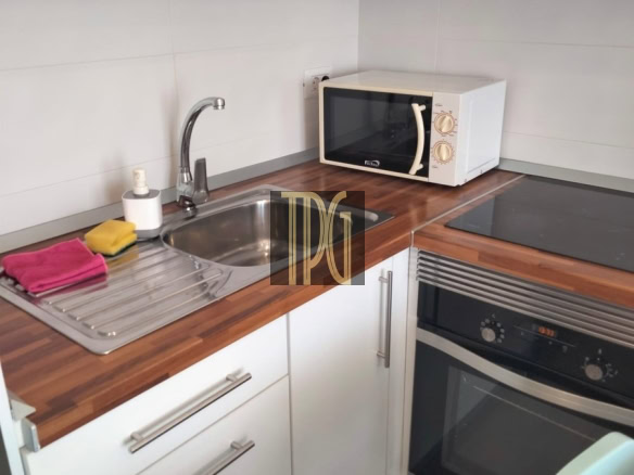 Compact kitchen corner with white cabinets, wooden countertop, sink, microwave, and built-in oven below it.