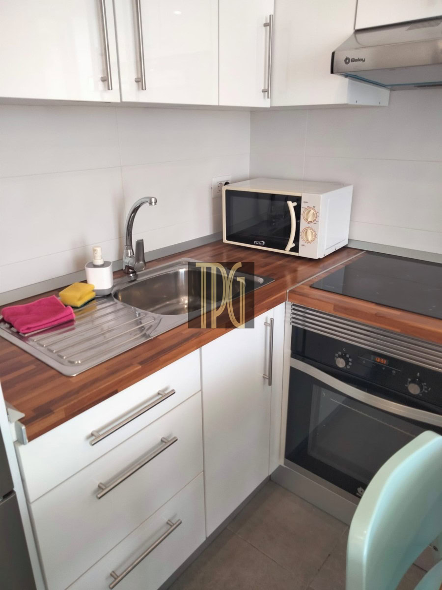 Compact kitchen corner with white cabinets, wooden countertop, sink, microwave, and built-in oven below it.