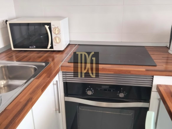 Compact kitchen setup with white cabinets, wood countertops, a microwave on the left, induction hob, and a built-in oven beneath a stainless range hood.