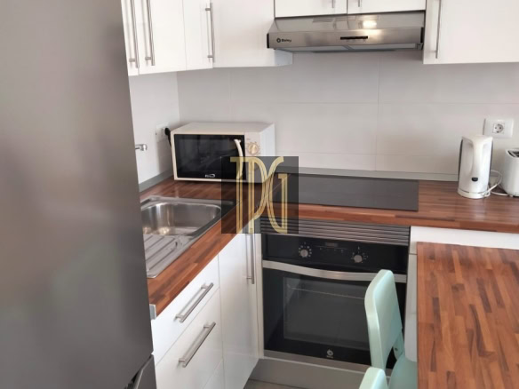 Compact L-shaped kitchen with white cabinets, stainless steel fridge, oven, and range hood on a wood countertop wall. (Informative)