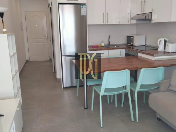 Modern open-plan kitchen with white glossy cabinets, stainless steel fridge, and a wooden island/bar area with mint teal chairs in front of a gray-tloor.