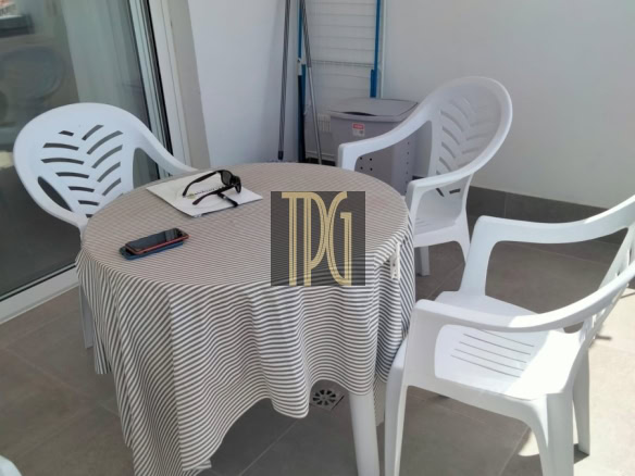 Patio balcony with a round striped table, four white plastic chairs, sunglasses, a phone on the table, and a drying rack in the background.