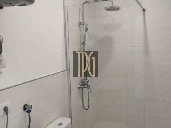Modern bathroom with glass shower enclosure, rainfall ceiling showerhead, handheld shower, toilet, and washing machine nearby.