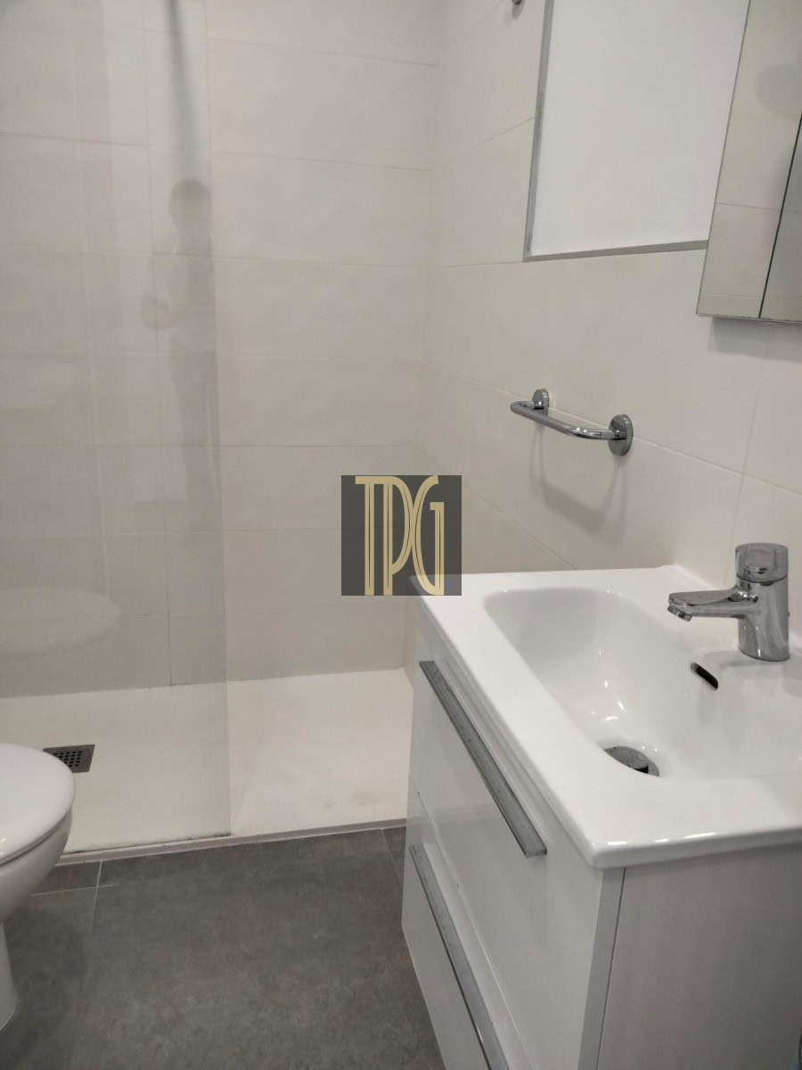 Modern white bathroom with glass shower, wall mirror cabinet, white sink vanity, chrome faucet, and towel rail.”,