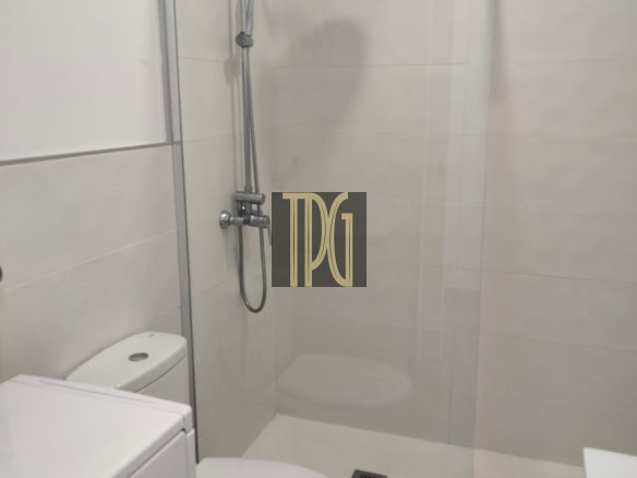 Modern bathroom with glass shower enclosure, rainfall showerhead, and nearby toilet and washing machine.