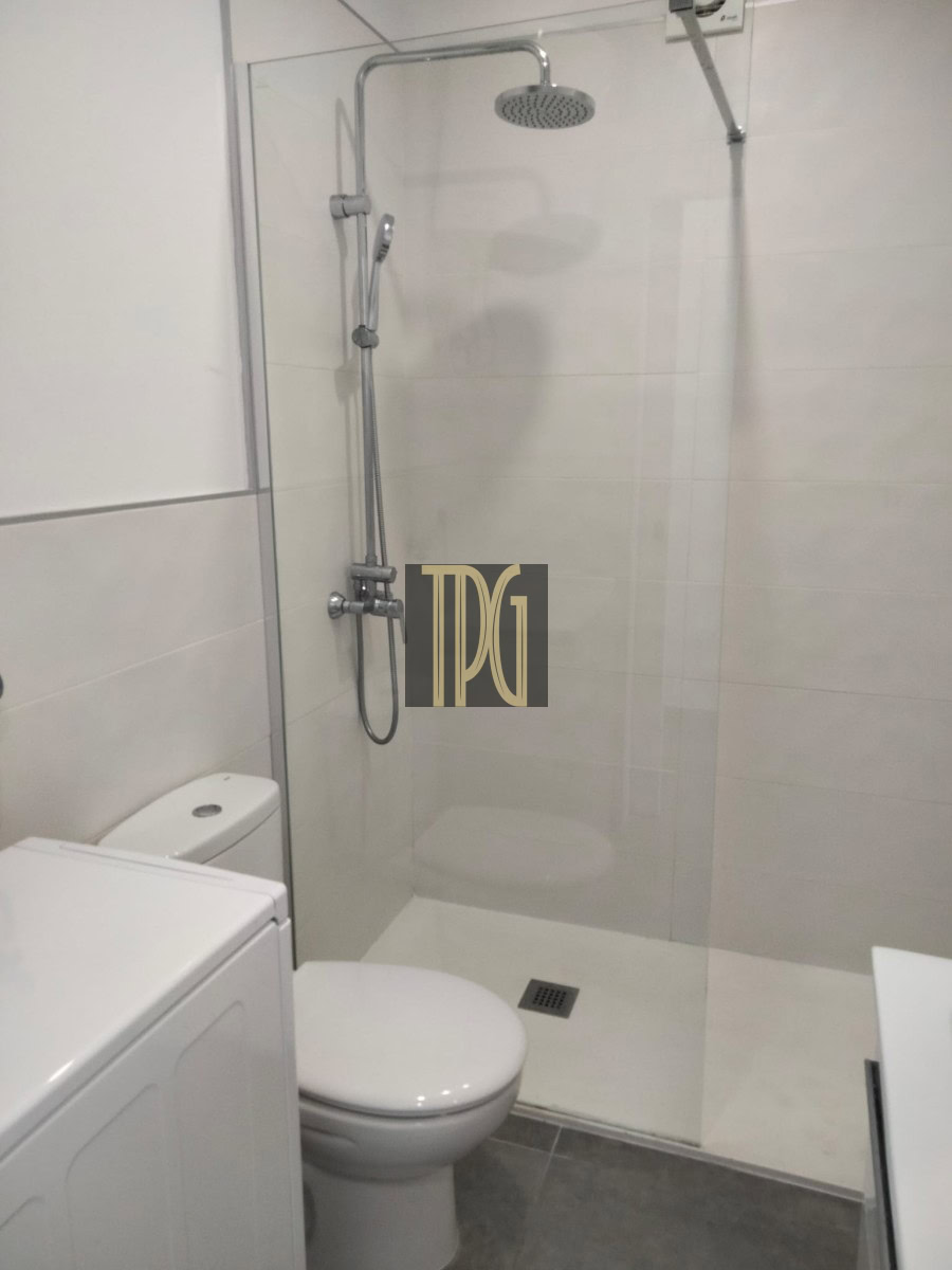 Modern bathroom with glass shower enclosure, rainfall showerhead, and nearby toilet and washing machine.