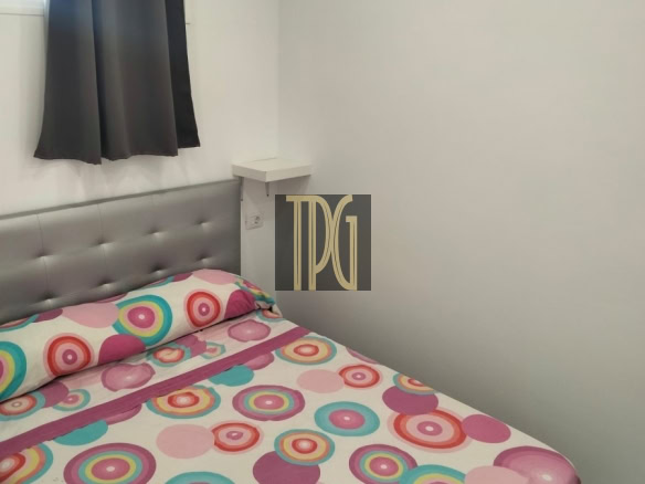 Small modern bedroom with a gray tufted headboard, white walls, and a bedspread of colorful circles (pink, teal, orange). Window with dark curtains nearby.