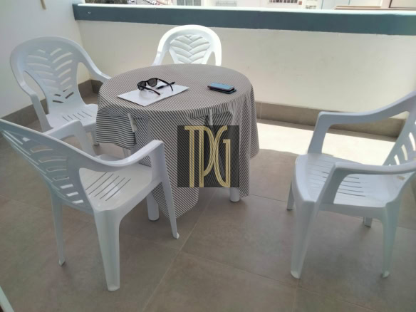 Outdoor balcony seating: five white plastic chairs around a round table with a striped tablecloth and items on the table (sunglasses, papers, and a phone).