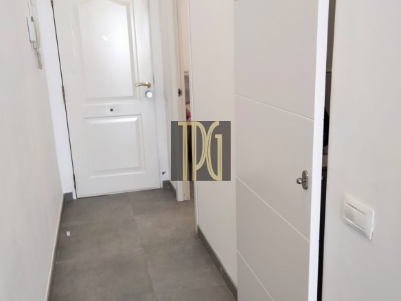 Narrow white hallway with grey tile floor, a closed white front door at the end, and a tall white sliding-door wardrobe on the right.